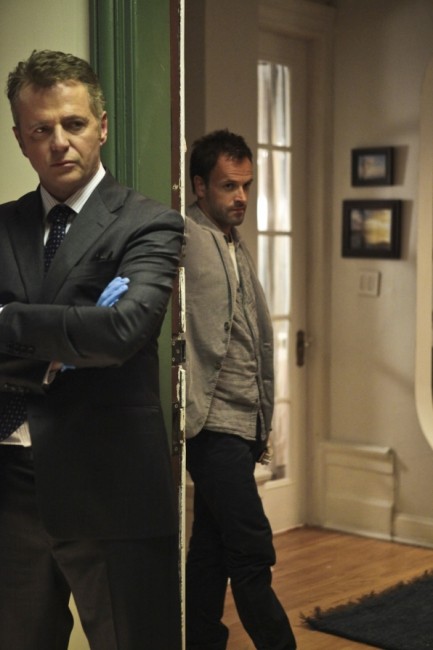 Gregson (Aidan Quinn) et Sherlock analysent tous les deux une scène de crime effroyable.